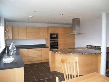 A kitchen with wooden cabinets black countertops and a wooden chair at Seabrook Broad Haven Pembrokeshire