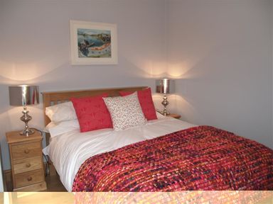 A bedroom with a bed with red and floral pillows and a multicolored blanket with two bedside tables with silver lamps and a painting on the wall at Seabrook in Broad Haven Pembrokeshire
