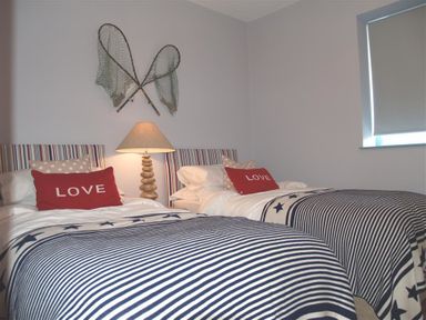 A bedroom with two single beds with striped bedding a illuminated lamp and fishing nets on the wall at Seabrook Broad Haven Pembrokeshire