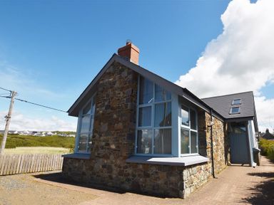 Stone cottage with large windows and blue trim under a blue sky at Seabrook in Broad Haven Pembrokeshire