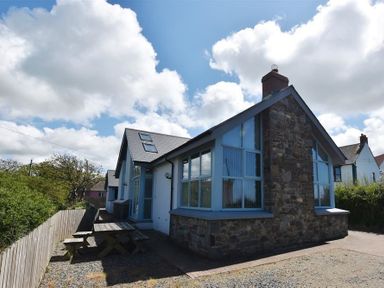 The exterior of a stone and white house with blue window frames and wooden picnic tables outside at Seabrook Broad Haven Pembrokeshire