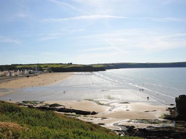 A wide sandy beach with people walking near water and houses along the shore at Seabrook in Broad Haven Pembrokeshire