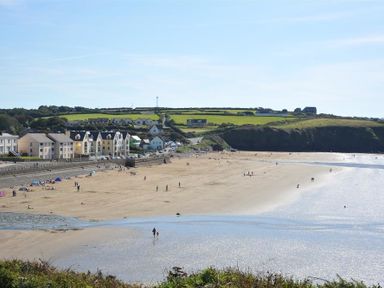 A sandy beach with people near the water and buildings along the shore at Seabrook in Broad Haven Pembrokeshire