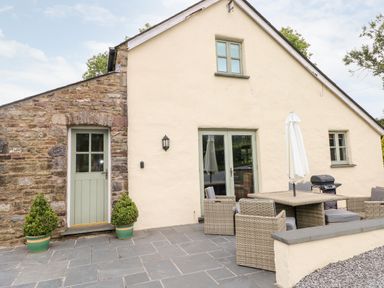 Exterior view of a stone and plaster house with green door and window frames patio with outdoor dining table chairs and umbrella at Gwyddno Lodge in Narberth Pembrokeshire