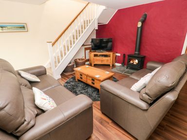 A living room with two brown sofas a wooden coffee table a TV on a wooden stand a wood burning stove and stairs at Gwyddno Lodge in Narberth Pembrokeshire