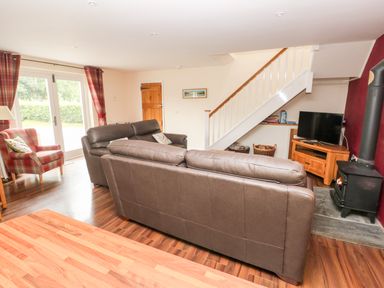 A living room with leather sofas a TV under stairs and a wood burning stove at Gwyddno Lodge in Narberth Pembrokeshire