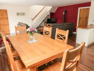 A dining table with six wooden chairs and a vase of flowers and a living room with sofas a TV and stairs at Gwyddno Lodge in Narberth Pembrokeshire