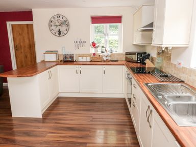 A kitchen with wooden countertops white cabinets a stainless steel sink an electric stove a window and various kitchen utensils at Gwyddno Lodge Narberth Pembrokeshire
