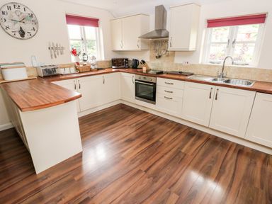 A kitchen with wooden countertops white cabinets stainless steel oven and range hood and two windows with red blinds at Gwyddno Lodge in Narberth Pembrokeshire