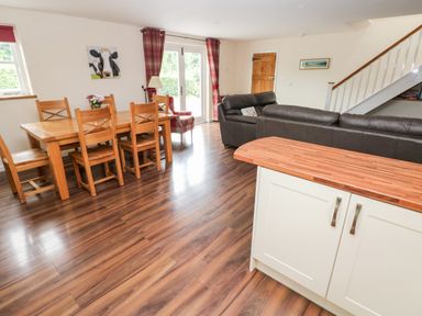 A dining area with wooden table and chairs next to a living room with leather sofas and a kitchen island at Gwyddno Lodge in Narberth Pembrokeshire