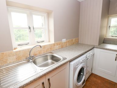 A kitchen with a stainless steel sink washing machine and dishwasher under a speckled countertop at Gwyddno Lodge in Narberth Pembrokeshire