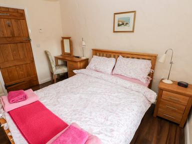 A bedroom with a bed with floral bedding two wooden bedside tables and a chair at Gwyddno Lodge in Narberth Pembrokeshire