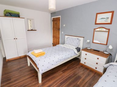 A bedroom with two single beds a dresser with lamps a wardrobe and a wooden door at Gwyddno Lodge Narberth Pembrokeshire