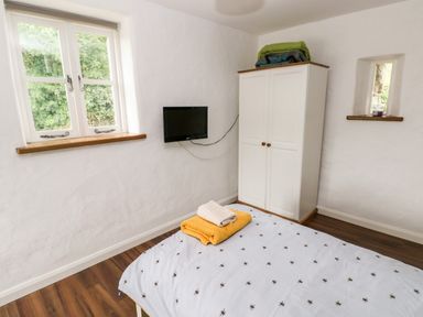 A bedroom with a bed, a white wardrobe, a wall-mounted tv, and two windows at Gwyddno Lodge in Narberth Pembrokeshire