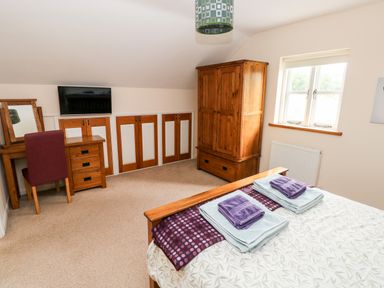 A bedroom with a bed and folded towels a wooden wardrobe a dressing table with a mirror a chair and a wall-mounted television at Gwyddno Lodge in Narberth Pembrokeshire