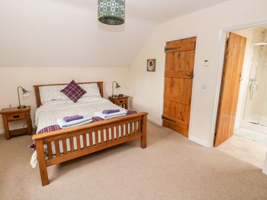 A bedroom with a wooden bed, bedside tables with lamps, and an open door leading to a bathroom at Gwyddno Lodge in Narberth Pembrokeshire