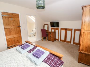 A bedroom with a wooden bed with folded towels on it a dressing table with a mirror and chair a television and wooden cupboards at Gwyddno Lodge in Narberth Pembrokeshire