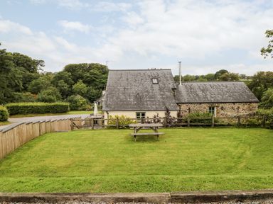 A backyard with a wooden picnic table a fenced garden and a house with a slate roof at Gwyddno Lodge in Narberth Pembrokeshire