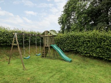 A children's wooden playset with swings and a slide in a grassy yard at Gwyddno Lodge in Narberth Pembrokeshire