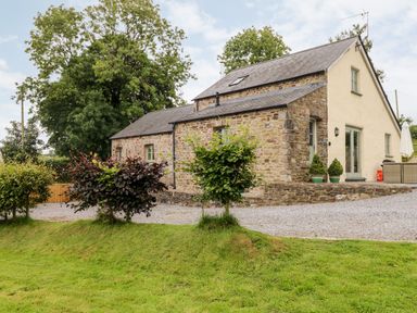 A stone and plaster cottage with a gravel driveway and small trees in the garden at Gwyddno Lodge in Narberth Pembrokeshire