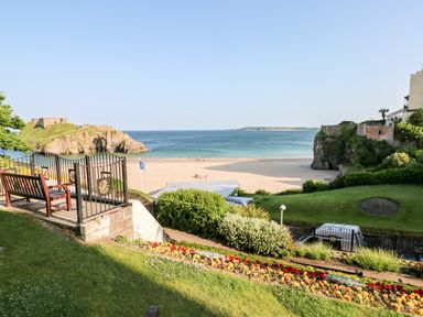 A garden with a bench overlooking a sandy beach and ocean with rocky cliffs at Gwyddno Lodge in Narberth Pembrokeshire