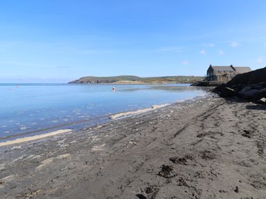 A sandy beach with calm water and a stone building on the right near the shore at End Cottage in Newport Pembrokeshire