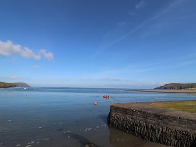 A coastal scene with a concrete pier a small boat on the water and land with grassy areas at End Cottage in Newport Pembrokeshire