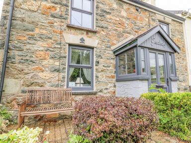 Stone house exterior with wooden bench shrubbery and enclosed porch at Greenbanks in Dinas Cross Pembrokeshire
