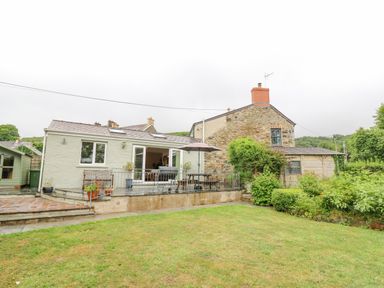 A backyard with a green lawn and a patio area next to a house with stone and plaster walls at Greenbanks in Dinas Cross Pembrokeshire