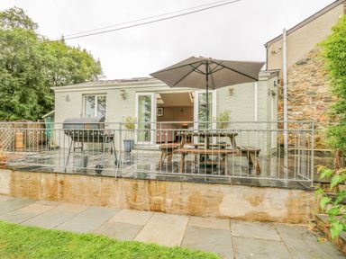 A patio with a barbecue grill a picnic table with an umbrella and potted plants outside a house at Greenbanks in Dinas Cross Pembrokeshire