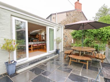 An outdoor patio with black tiled floor a wooden picnic table with umbrella and potted plants outside French doors at Greenbanks in Dinas Cross Pembrokeshire