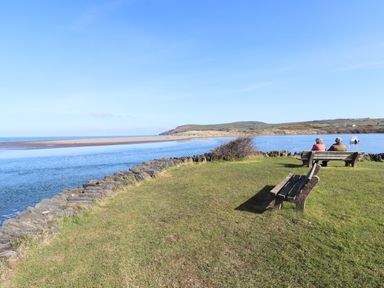 Two people sitting on a bench near a body of water with grassy land and hills in the background at Middle Cottage in Newport Pembrokeshire