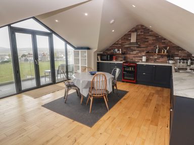 A kitchen and dining area with a wooden floor a round table with chairs and large windows showing outside at The Willows in Newport Pembrokeshire