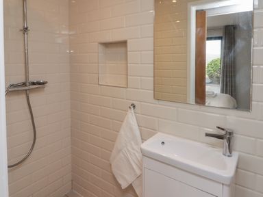 A bathroom shower area with white tiled walls a wall niche a towel on a hook a white sink with a faucet and a mirror reflecting a window at The Willows Newport Pembrokeshire