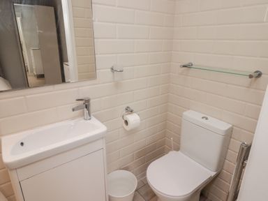A bathroom with a white sink cabinet mirror toilet roll holder and glass shelf at The Willows in Newport Pembrokeshire