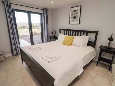 A bedroom with a black bed frame white bedding yellow pillow bedside tables with lamps and glass doors at The Willows in Newport Pembrokeshire