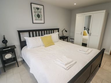 A bedroom with a black bed frame white bedding yellow pillow two bedside tables and a white wardrobe with mirror at The Willows in Newport Pembrokeshire