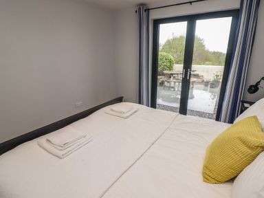 A bedroom with a bed towel sets and a yellow pillow next to glass doors with blue curtains at The Willows in Newport Pembrokeshire