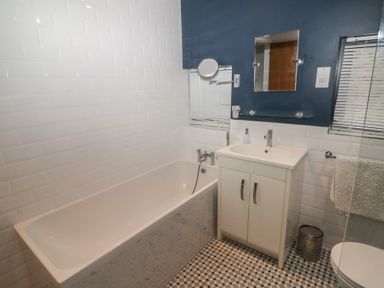 A bathroom with a bathtub a sink with cabinet a mirror and patterned floor tiles at The Willows in Newport Pembrokeshire
