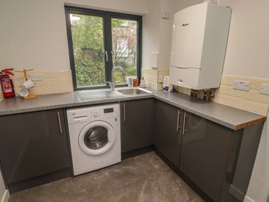 A laundry room with a washing machine a sink countertop cabinets and a window at The Willows in Newport Pembrokeshire