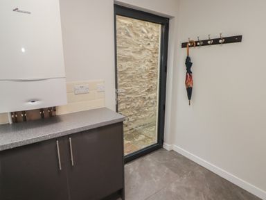 A utility room with a countertop cabinet boiler electric sockets umbrella on a wall hook and glass door showing stone wall outside at The Willows in Newport Pembrokeshire