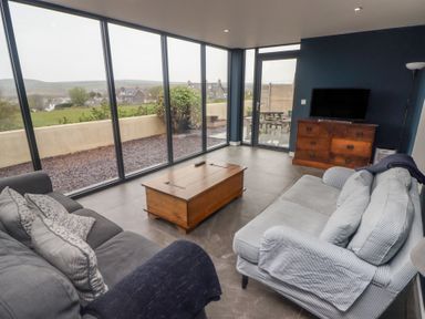 A living room with sofas a wooden coffee table a chest of drawers and large glass windows at The Willows in Newport Pembrokeshire