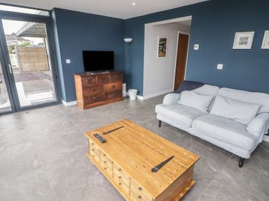 A living room with a wooden TV stand and coffee table a gray sofa and glass door at The Willows in Newport Pembrokeshire