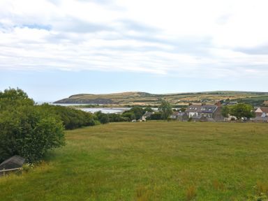 A grassy field with trees and houses overlooking a body of water and hills in the distance at The Willows in Newport Pembrokeshire