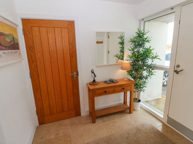 An entryway with a wooden door a white door with glass a wooden console table with drawers a lamp a potted plant and a wall mirror at Gwelfor Marloes in Marloes Pembrokeshire