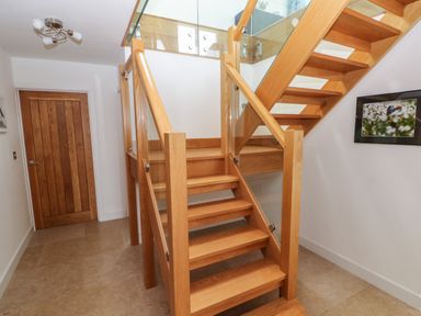 A wooden staircase with glass panels in a hallway with a wooden door and a framed picture on the wall at Gwelfor Marloes in Marloes Pembrokeshire