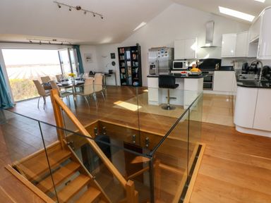 An open plan kitchen and dining area with a glass railing stairwell and a dining table with chairs at Gwelfor Marloes in Marloes Pembrokeshire