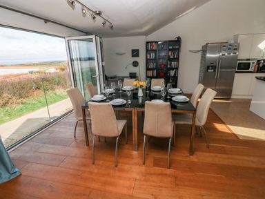 A dining area with a set table for eight people and glass doors opening to an outdoor view at Gwelfor Marloes in Marloes Pembrokeshire