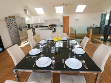 A dining table set with plates glasses and cutlery in a kitchen with white cabinets and a stainless steel fridge at Gwelfor Marloes in Marloes Pembrokeshire