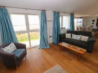 A living room with blue curtains a dark sofa and a wooden coffee table at Gwelfor Marloes in Marloes Pembrokeshire
